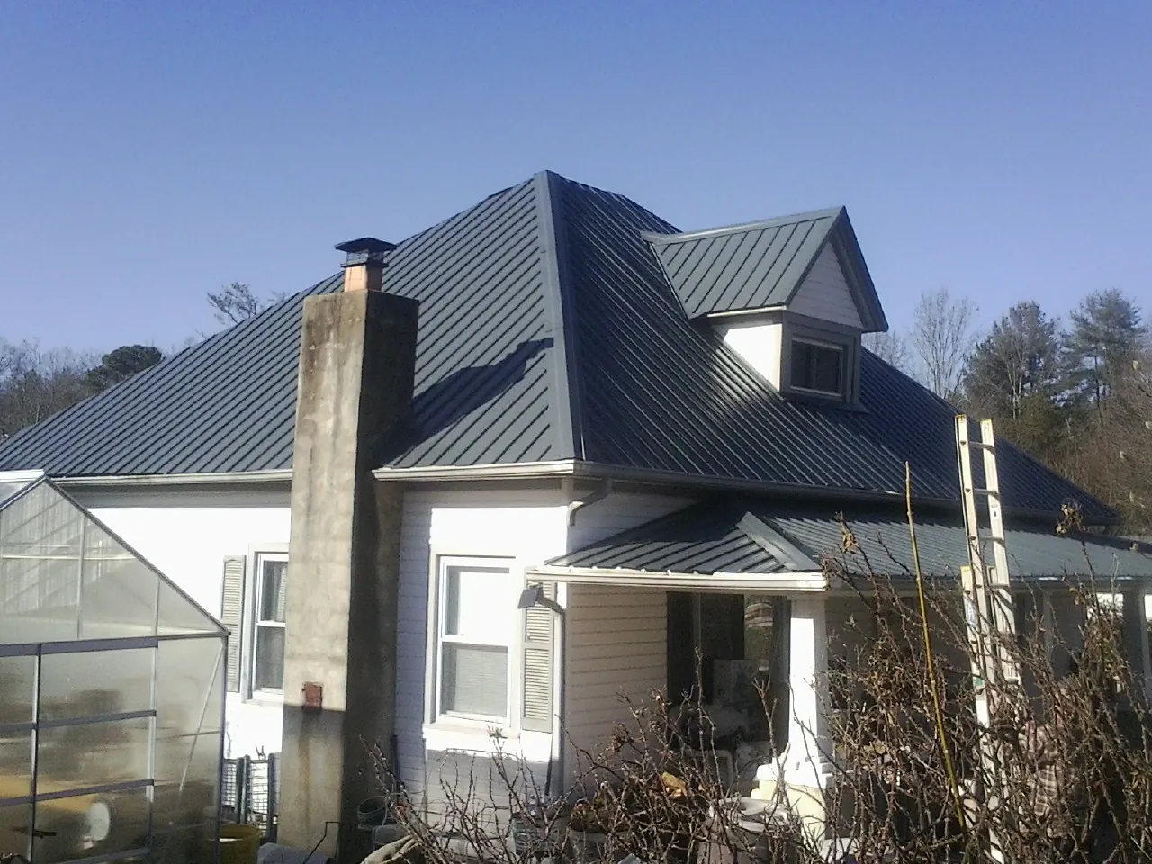 Dark blue standing seam metal roof on a white farmhouse with dormer — Slate & Tile Roof Repair by Roofing Brothers in Rock Rapids