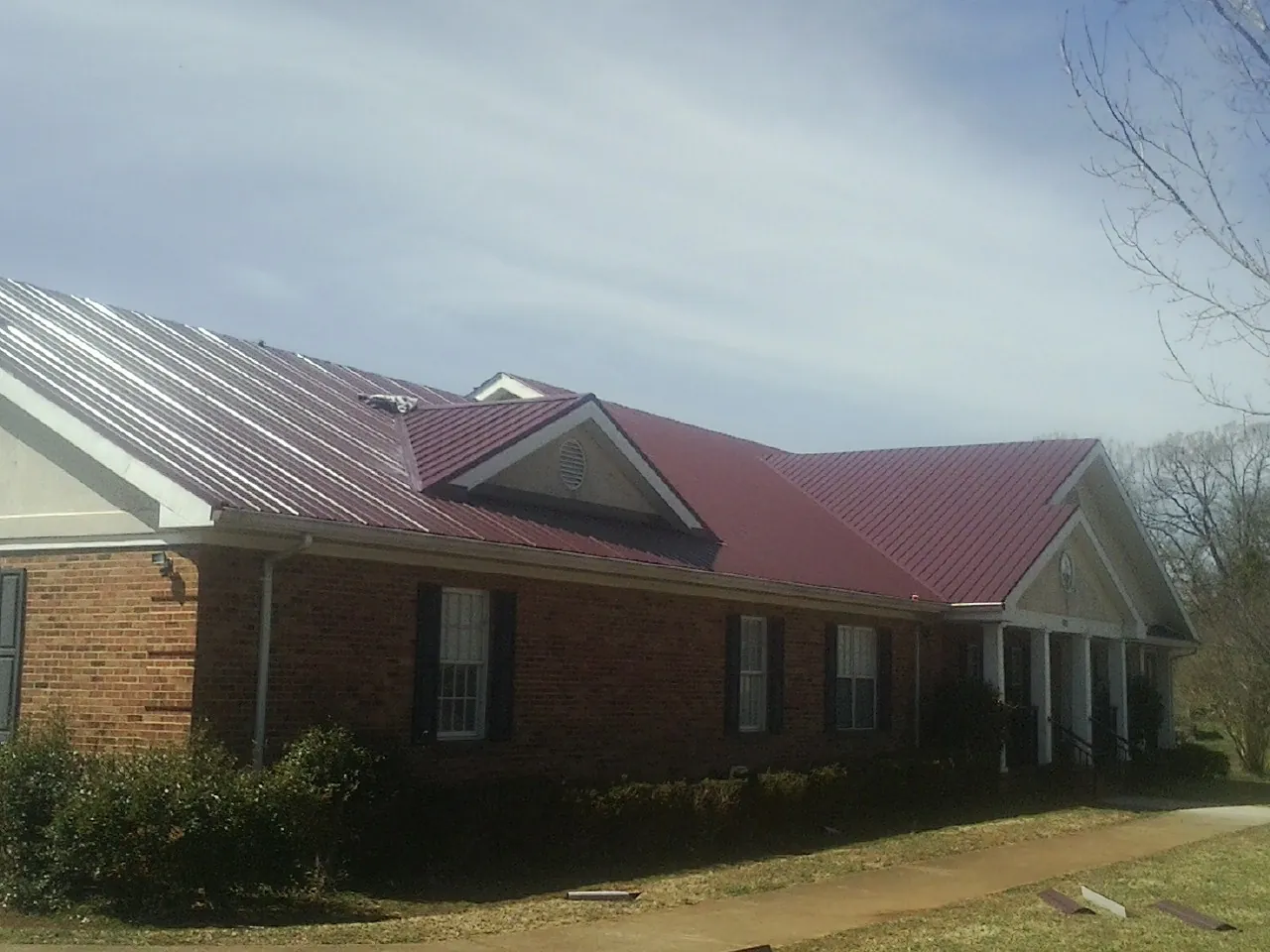 Red metal roof with gabled entries on a long brick building, from a Hail Damage Roof Repair job in Rock Rapids