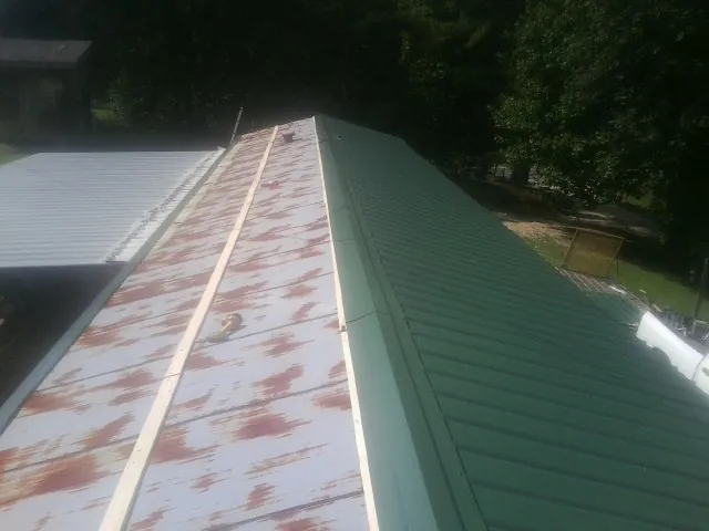 Old rusted panels beside newly installed green metal roofing — Wind Damage Roof Repair by Roofing Brothers in Rock Rapids