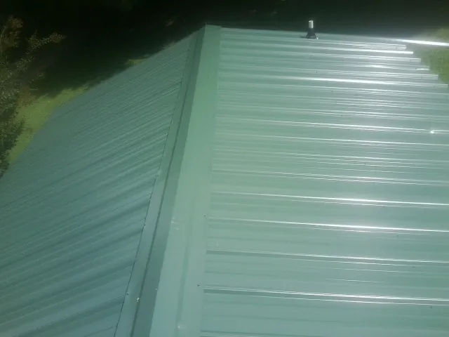 New green metal panels meeting at the ridge of a roof — Flat Roof Repair work by our crew in Rock Rapids