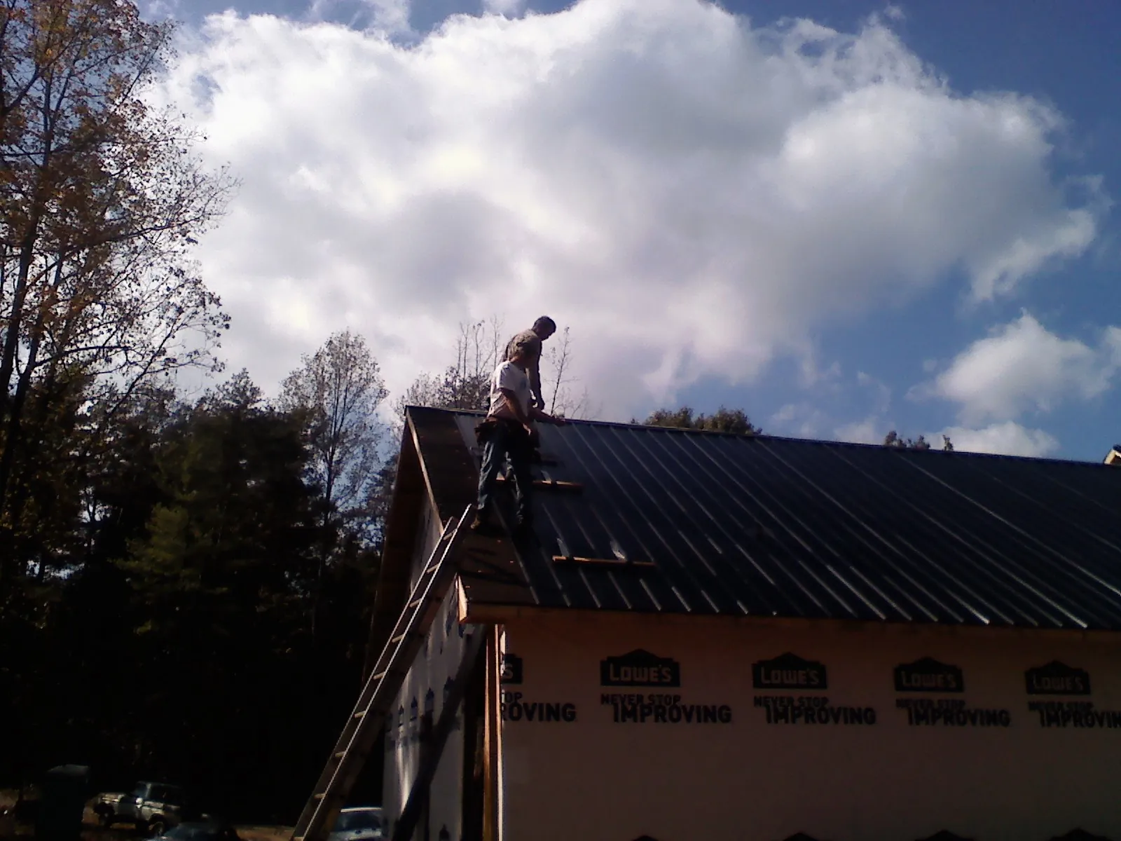 Roofer fastening dark metal panels high against a cloudy sky, from a Roof Inspection job in Rock Rapids