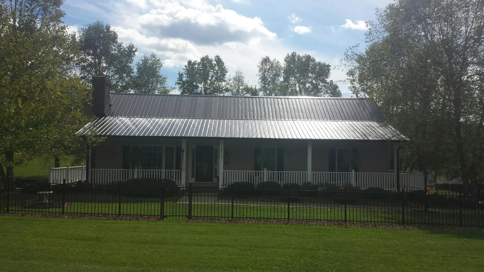 Gray metal roof on a brick ranch with a full width front porch — Gutter Guard Installation work by our crew in Rock Rapids