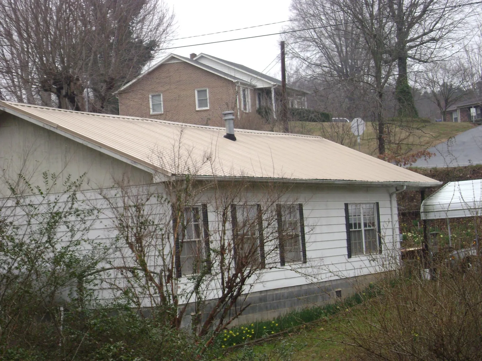 Tan metal roof on a white sided house set into a hillside — Commercial Roofing by Roofing Brothers in Rock Rapids